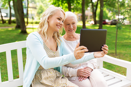 family, technology and people concept - happy smiling young daughter with tablet pc computer and senior mother sitting on park bench