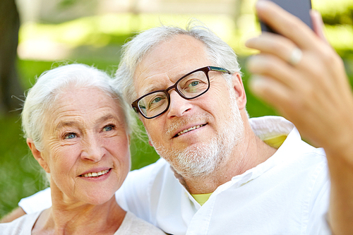 technology, relationship and old people concept - happy senior couple with smartphone taking selfie and hugging in summer