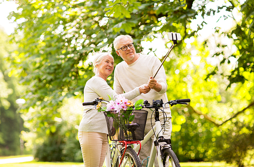 active old age, technology and lifestyle concept - happy senior couple walking with fixie bicycles taking selfie by smartphone at summer park