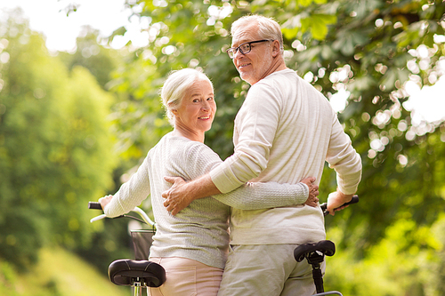 old age, people and lifestyle concept - happy senior couple with bicycles hugging at summer city park