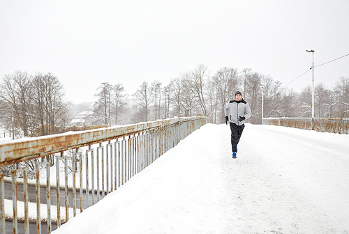 fitness, sport, people, season and healthy lifestyle concept - young man running along snow covered winter bridge road