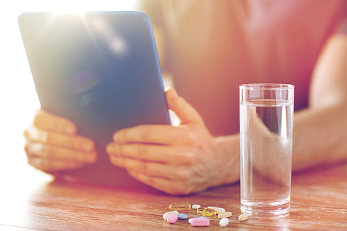 medicine, technology, nutritional supplements and people concept - close up of male hands with tablet pc computer, pills and water on table