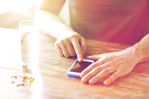 medicine, technology, nutritional supplements and people concept - close up of male hands pointing finger to blank smartphone screen, pills and water on table