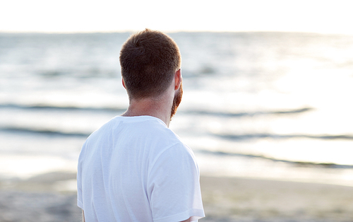 people concept - young man in white t-shirt on beach looking at sea