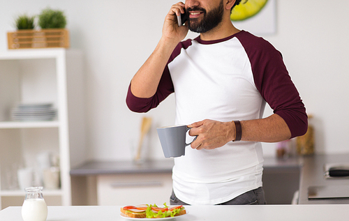 lifestyle, technology and people concept - man having sandwiches with coffee for breakfast and calling on smartphone at home kitchen