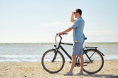 people, leisure and lifestyle concept - happy young man with bicycle on beach