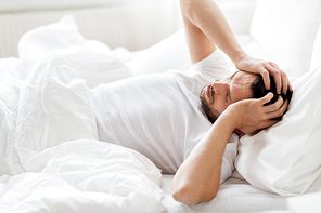 people, bedtime and rest concept - man lying in bed at home suffering from headache or hangover