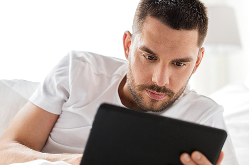 technology, internet, communication and people concept - close up of young man with tablet pc computer in bed at home