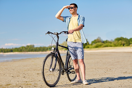 people, leisure and lifestyle concept - happy young man with bicycle on summer beach