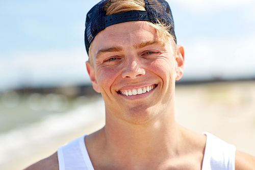 summer holidays, portrait and people concept - close up of happy smiling young man in cap on beach