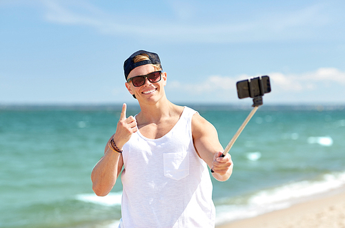 summer holidays and people concept - happy smiling young man with smartphone selfie stick taking picture on beach