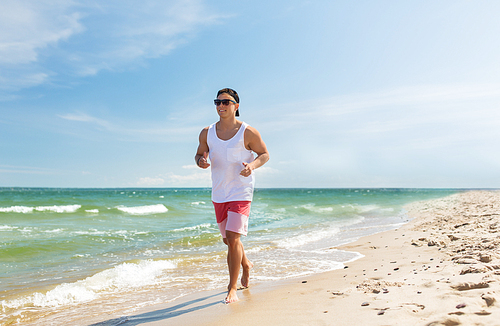 fitness, sport, people and healthy lifestyle concept - happy young man running along summer beach