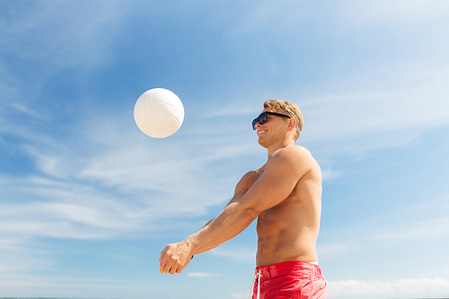 summer, sport, fitness and people concept - young man with ball playing volleyball on beach