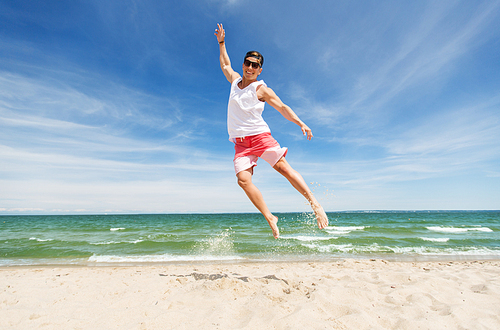 summer holidays and people concept - happy smiling young man jumping on beach