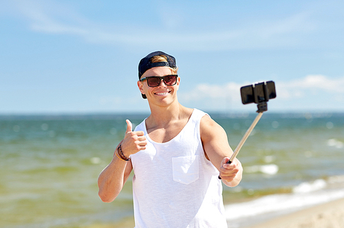 summer holidays and people concept - happy smiling young man with smartphone selfie stick taking picture on beach