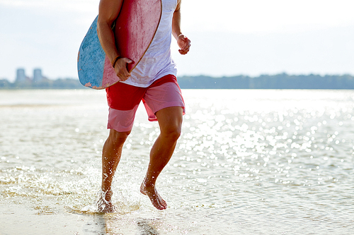 skimboarding, water sport and people concept - happy smiling young man with skimboard on summer beach