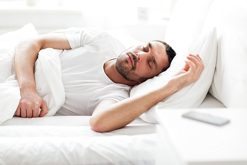 people, bedtime and rest concept - man sleeping in bed at home with smartphone on nightstand