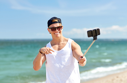 summer holidays and people concept - happy smiling young man with smartphone selfie stick taking picture on beach