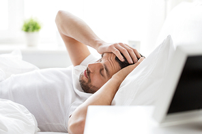 people, bedtime and rest concept - man lying in bed at home suffering from headache or hangover