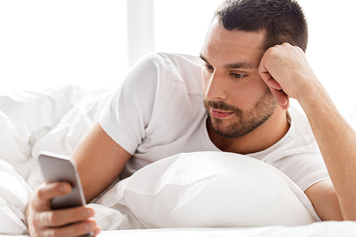 technology, internet, communication and people concept - close up of young man texting on smartphone in bed at home in morning