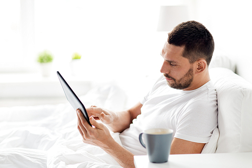 technology, internet, communication and people concept - young man with tablet pc computer in bed at home bedroom