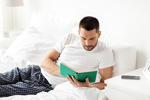 people and rest concept - man reading book in bed at home