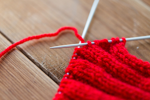 handicraft and needlework concept - close up of hand-knitted item with knitting needles on wood
