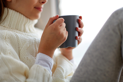 hot drinks and people concept - beautiful girl in winter sweater with tea mug sitting at home window