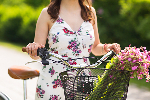 people, leisure and lifestyle concept - close up of young woman wearing summer dress with fixie bicycle and wild flowers in vintage basket at park