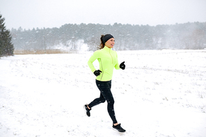 fitness, sport, people, season and healthy lifestyle concept - happy woman running along snow covered winter road