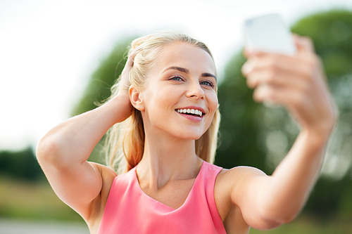 technology and people concept - happy young beautiful woman with smartphone taking selfie outdoors