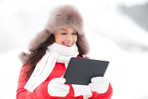 people, technology and leisure concept - happy smiling woman in winter fur hat with tablet pc computer outdoors