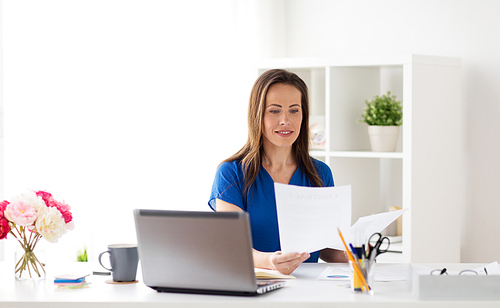business, people and work concept - happy smiling woman with laptop computer working and writing to notebook at office or home