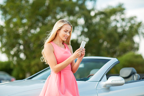 road trip, technology and communication concept - happy young woman with smartphone at convertible car