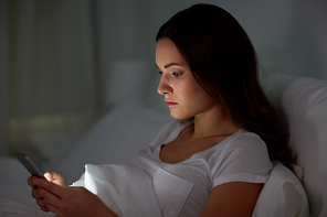 technology, internet, communication and people concept - young woman with smartphone in bed at home at night