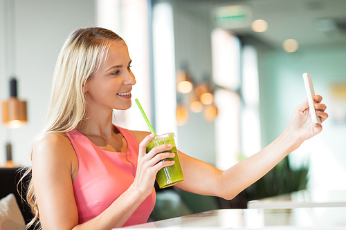 technology, people and leisure concept - happy woman with smartphone and smoothie drink or vegetarian shake taking selfie at restaurant