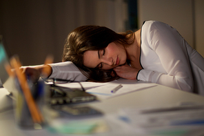 business, overwork, deadline and people concept - tired woman with laptop and papers sleeping on table at night office