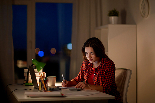 people, education, freelance and learning concept - student girl with notebook and calculator doing math at home at night