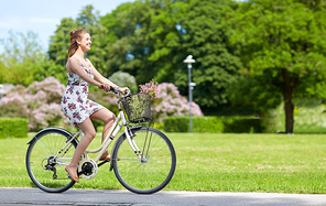 people, leisure and lifestyle - happy young hipster woman wearing summer dress riding fixie bicycle with wild flowers in basket at park
