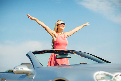 travel, summer holidays, road trip and people concept - happy young woman wearing sunglasses in convertible car enjoying sun