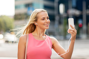 technology, lifestyle and people concept - smiling young woman with smartphone and earphones listening to music and taking selfie in city