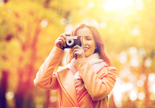 season, photography and people concept - beautiful happy young woman taking picture with vintage camera in autumn park
