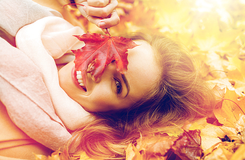season and people concept - beautiful young woman with autumn maple leaf lying on ground