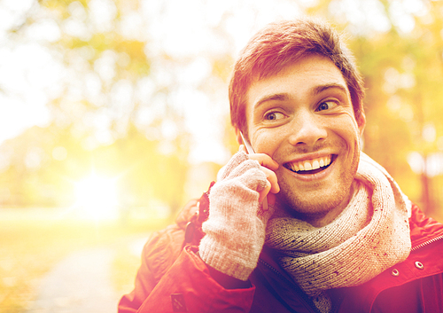 leisure, technology, communication and people concept - happy smiling young man calling on smartphone at autumn park