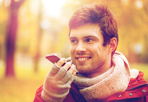 leisure, technology, communication and people concept - smiling hipster man using voice command recorder or calling on smartphone at autumn park