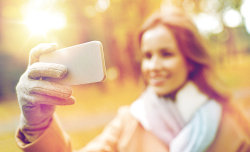 season, technology and people concept - beautiful young happy woman taking selfie with smartphone in autumn park