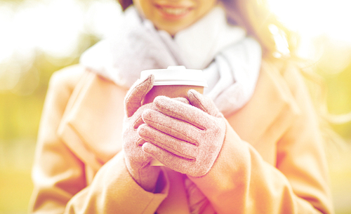 season, hot drinks and people concept - close up of beautiful happy young woman drinking coffee or tea from disposable paper cup in autumn park