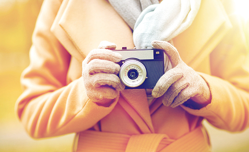 season, photography and people concept - close up of young woman taking picture with vintage camera in autumn park