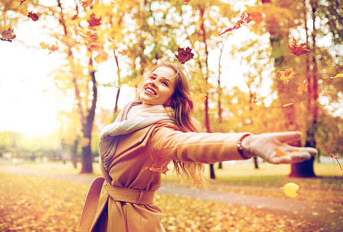 season and people concept - beautiful happy young woman having fun with leaves in autumn park