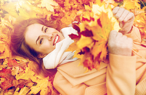 season and people concept - beautiful young woman with autumn maple leaves lying on ground